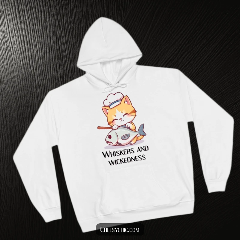Funny hoodie with a cute cat wearing a mini chef hat, batting at a rolling fish, cozy and humorous.